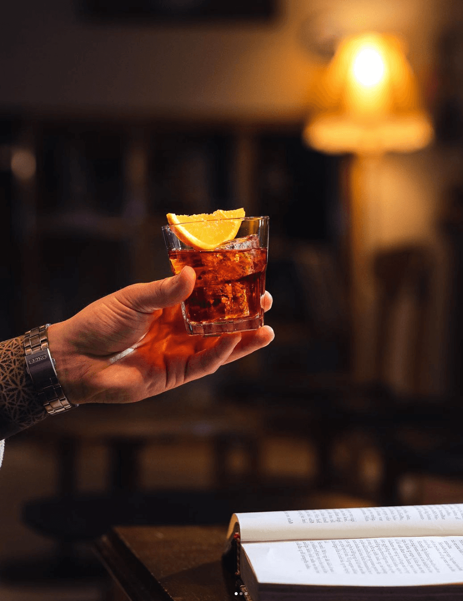 A hand holding a cocktail beside a book